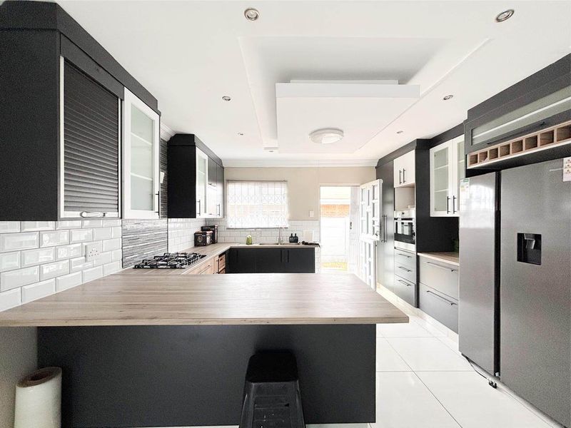 Modern kitchen featuring dark cabinetry, subway tile backsplash, gas hob, built-in oven, and a breakfast bar with light wood-look countertops.