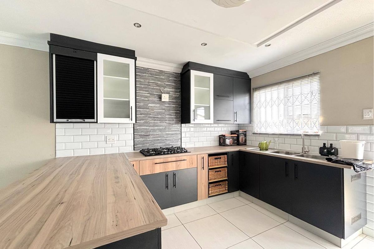 Modern kitchen featuring dark cabinetry, wood-look laminate countertops, subway tile backsplash, gas hob, and tiled flooring with ample workspace.