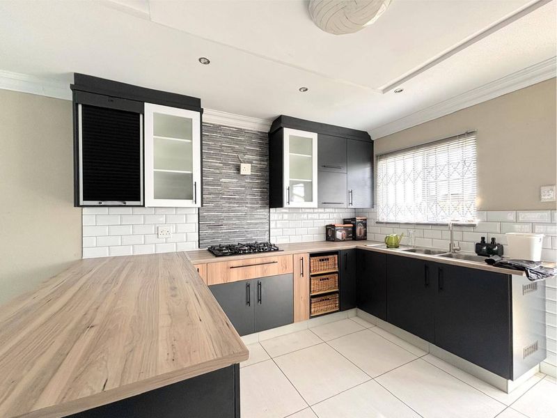Modern kitchen featuring dark cabinetry, wood-look laminate countertops, subway tile backsplash, gas hob, and tiled flooring with ample workspace.