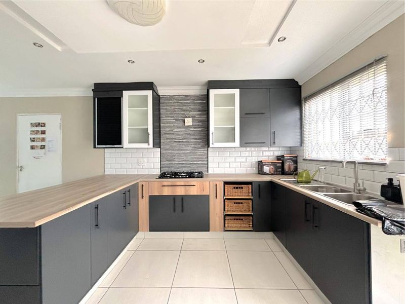 Modern kitchen featuring dark grey and wood-tone cabinetry, subway tile backsplash, gas hob, and light-colored floor tiles with ample counter space.