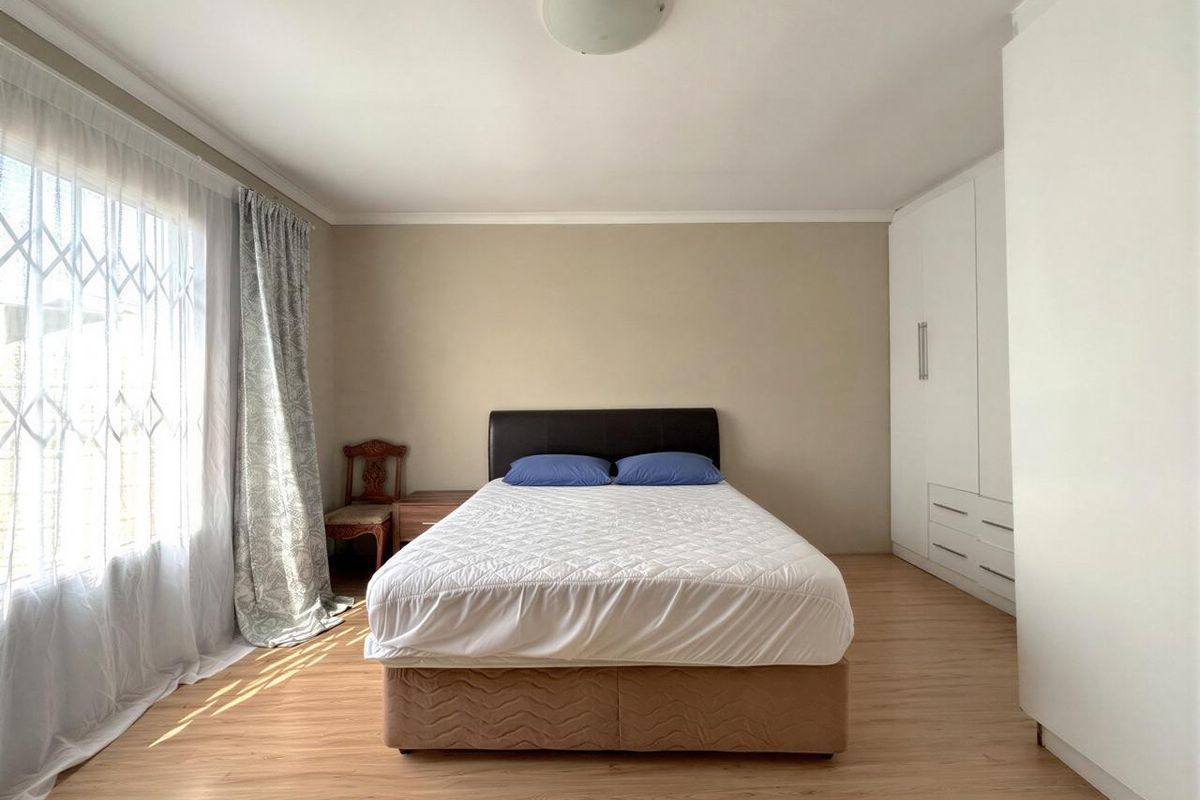 A well-maintained bedroom featuring light laminate flooring, neutral walls, and ample built-in cupboard storage.