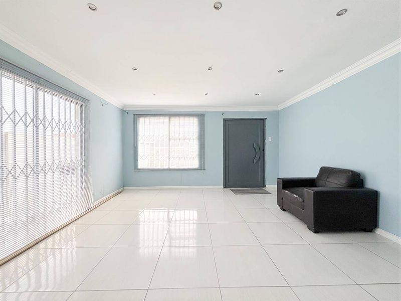 Spacious living room featuring neutral tiled flooring, recessed downlighting, and large sliding doors with security gates, offering a bright and open layout.