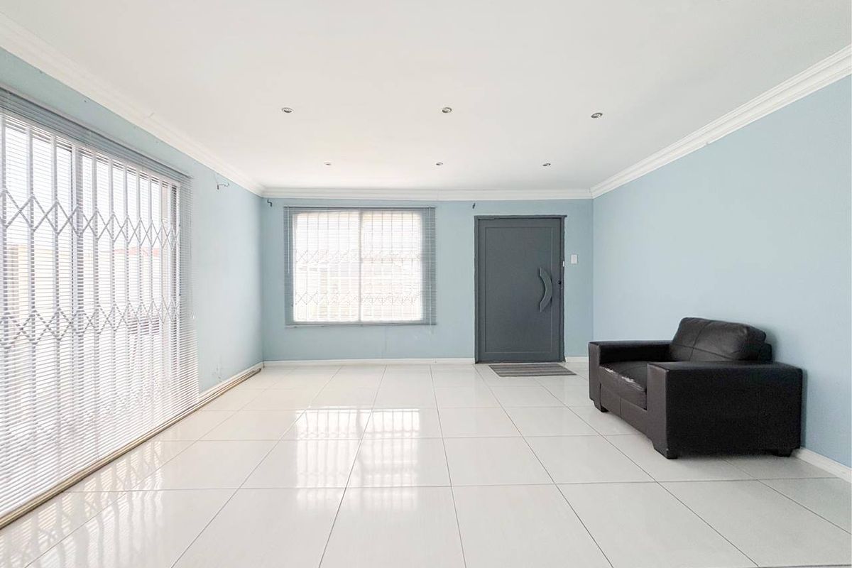 Spacious living room featuring neutral tiled flooring, recessed downlighting, and large sliding doors with security gates, offering a bright and open layout.