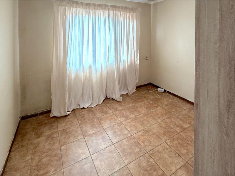 An empty bedroom featuring tiled flooring and a window with curtains, presenting a blank canvas for potential renovation or staging.