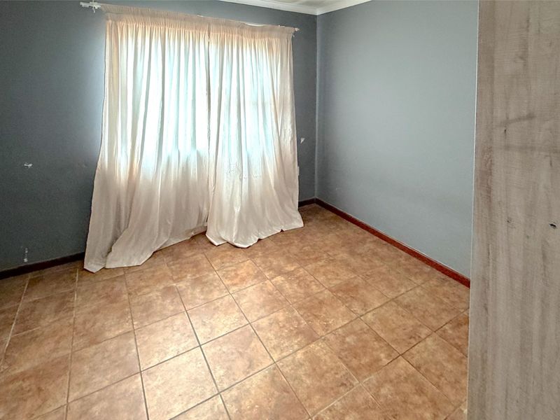 An empty bedroom featuring tiled flooring and neutral grey walls, providing a blank canvas for personalization.