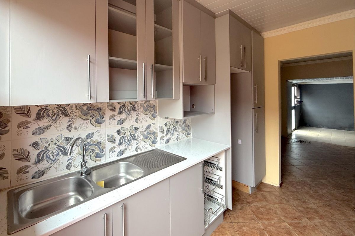A functional kitchen featuring modern grey cabinetry, stone countertops, a double sink, and a decorative floral tile backsplash.