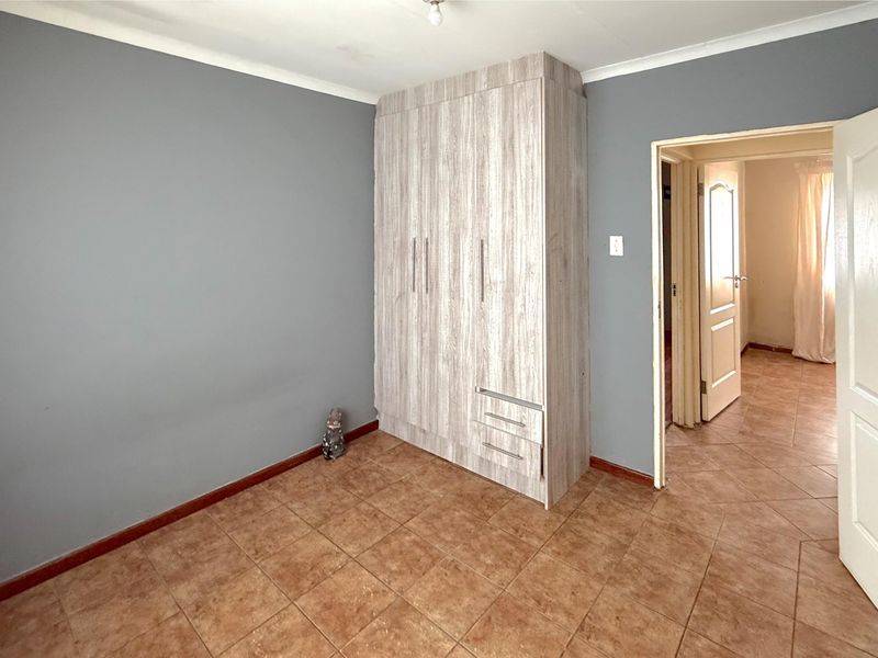 A bedroom featuring tiled flooring, grey painted walls, and a built-in wooden wardrobe with integrated drawers.