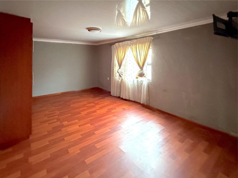 A spacious bedroom featuring laminate flooring, a built-in cupboard, and a glossy ceiling finish, offering a blank canvas for personalization.