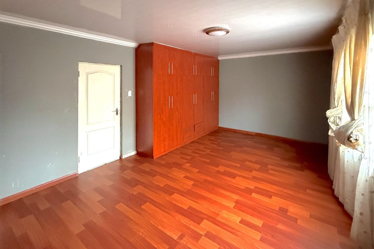 Spacious bedroom featuring warm-toned laminate flooring, built-in wooden cupboards, and neutral grey walls with classic cove cornicing.