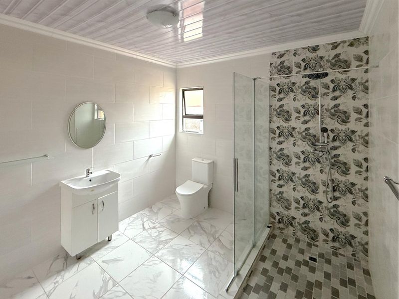 Modern bathroom featuring a glass-enclosed shower with decorative tiled accent wall, vanity basin, and clean white floor tiling.