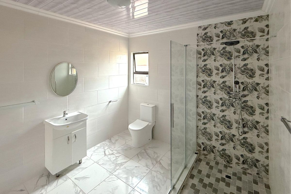 Modern bathroom featuring a glass-enclosed shower with decorative tiled accent wall, vanity basin, and clean white floor tiling.