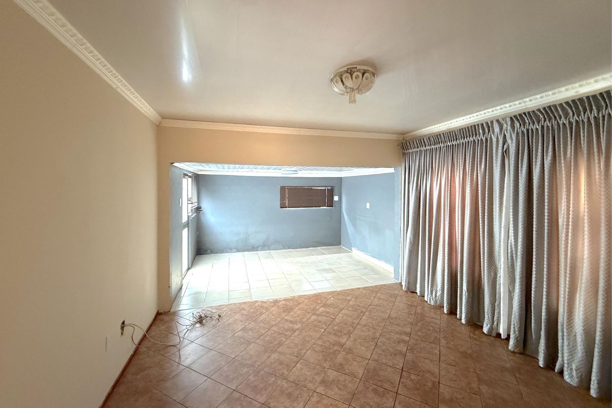 An empty living room featuring ceramic tile flooring, crown molding, and a connected secondary space with tiled floors and wall-mounted window.