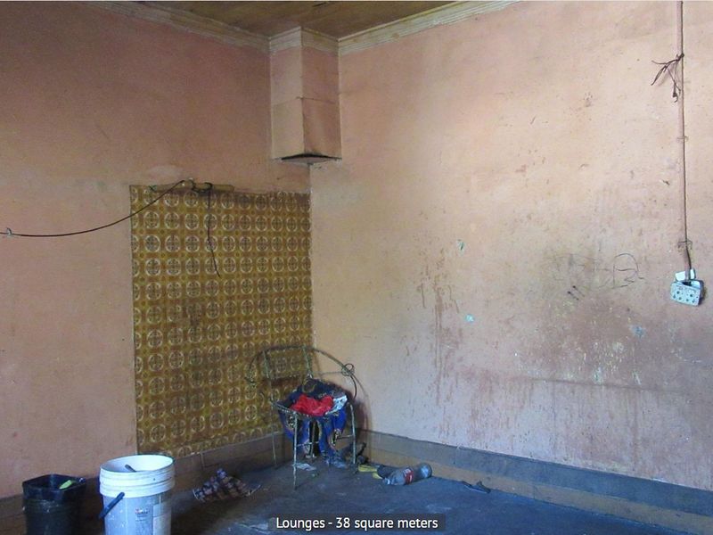 A spacious, empty living room requiring significant renovation, featuring worn wall finishes and exposed electrical fixtures.