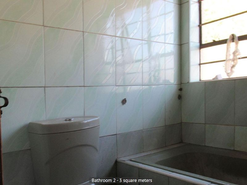 A compact bathroom featuring a built-in bathtub, toilet, and light-colored ceramic wall tiles, requiring some maintenance and cosmetic updates.