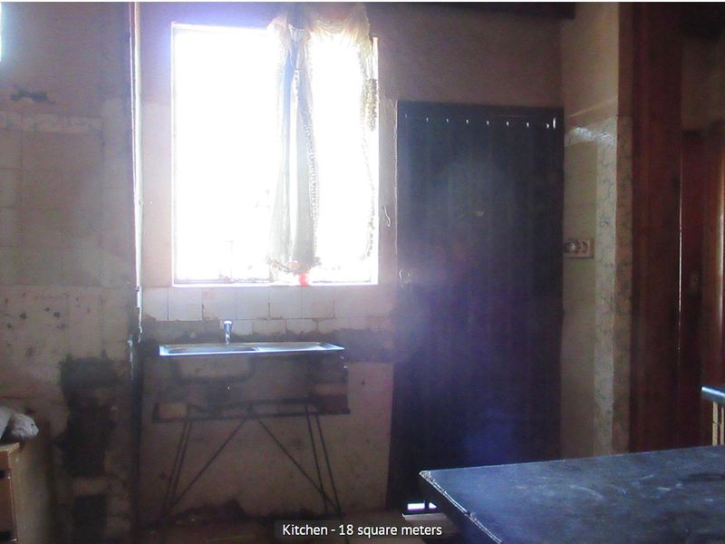 A dated kitchen space featuring a stainless steel sink, tiled splashback, and built-in countertop, currently requiring significant renovation and cosmetic repairs.