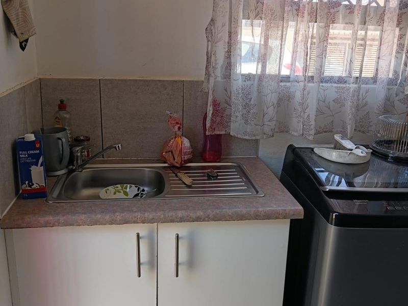 A functional scullery area featuring a stainless steel sink, laminate countertop, and built-in cabinetry, with a window fitted with a security gate.