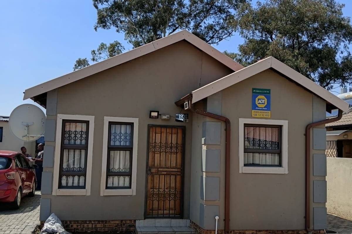 Front elevation of a single-story house featuring a paved driveway, security gate, and security bars on windows.
