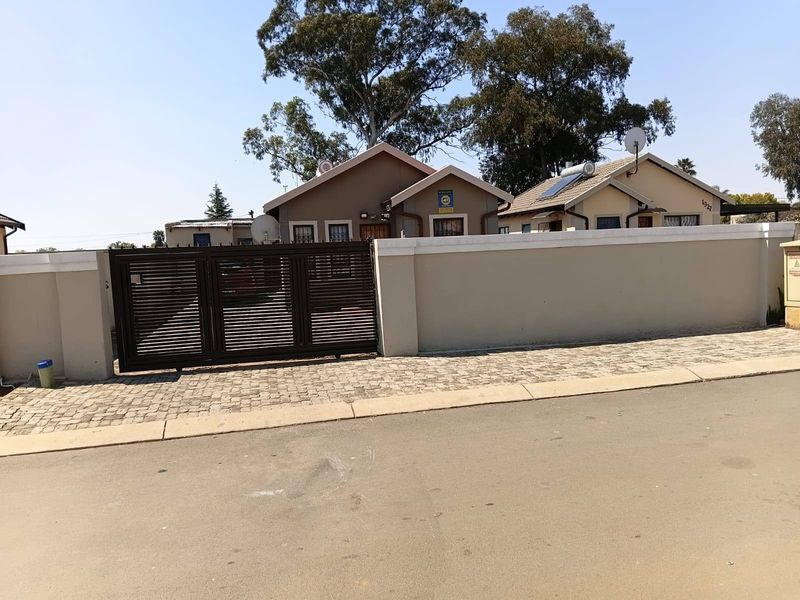 Front view of the property featuring a secure perimeter wall, sliding driveway gate, and paved entrance area.