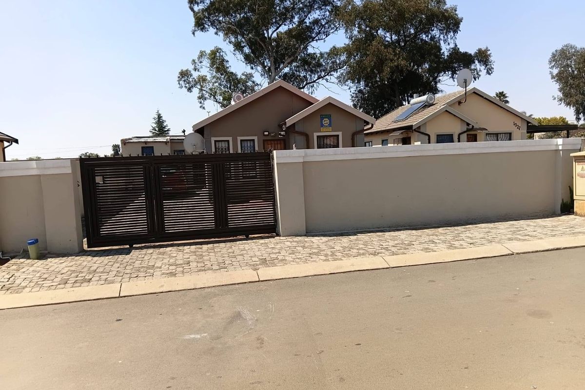 Front view of the property featuring a secure perimeter wall, sliding driveway gate, and paved entrance area.