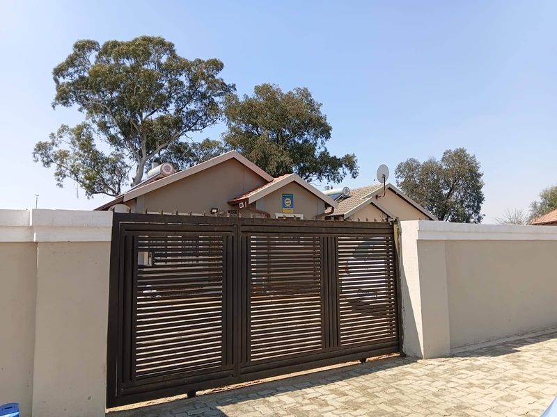 Front view of the property featuring a secure perimeter wall, sliding gate, paved driveway, and solar geyser installation on the tiled roof.