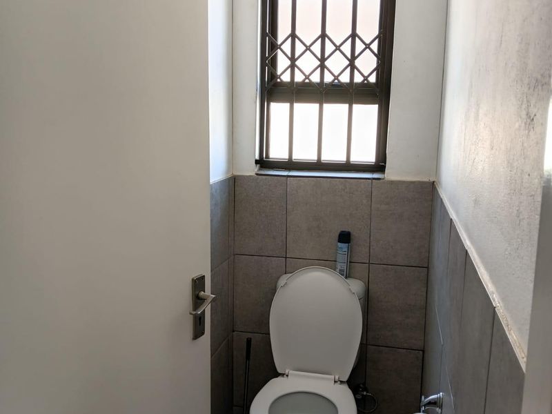 A compact guest bathroom featuring neutral wall and floor tiling, a standard toilet, and a window fitted with a security gate.
