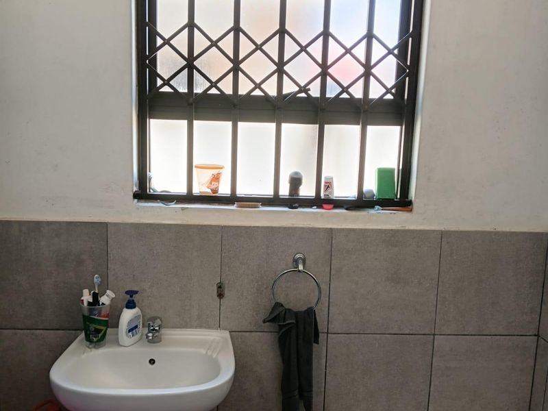 A functional bathroom featuring a pedestal washbasin, a bathtub, and a window fitted with a security gate.