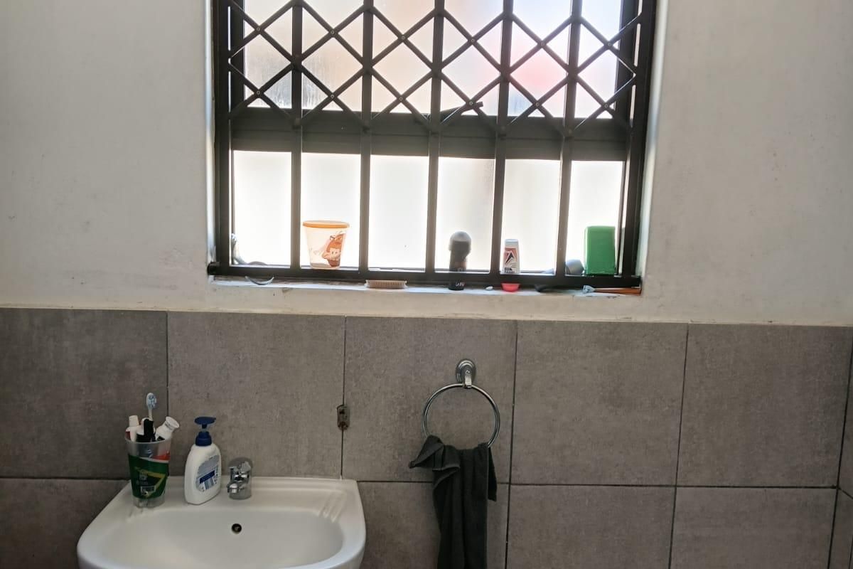 A functional bathroom featuring a pedestal washbasin, a bathtub, and a window fitted with a security gate.