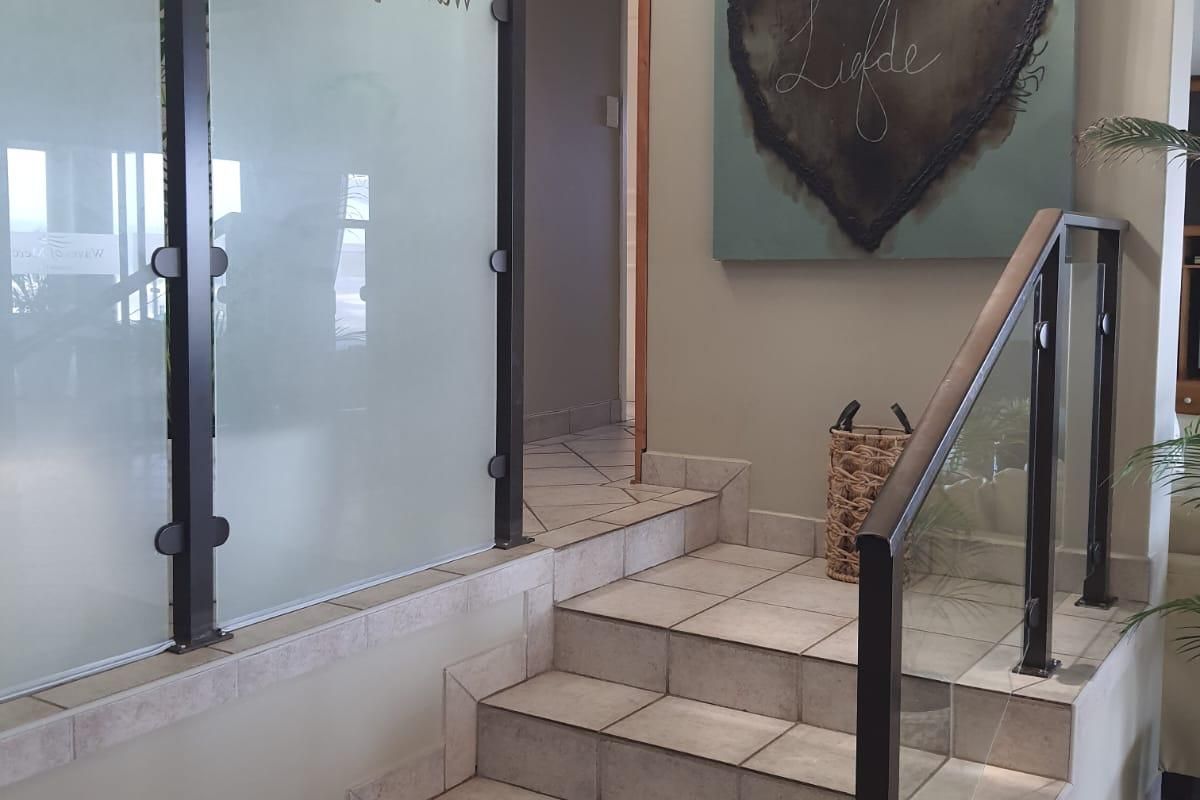 An inviting entrance area featuring a tiled staircase with a modern glass and metal balustrade and a decorative frosted glass partition.