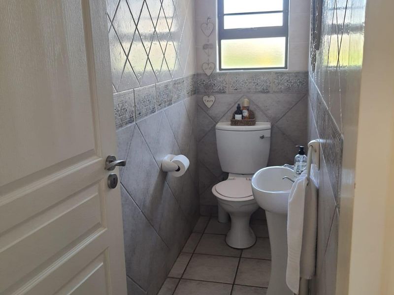 A compact guest bathroom featuring a pedestal basin, toilet, and neutral tiled finishes throughout.