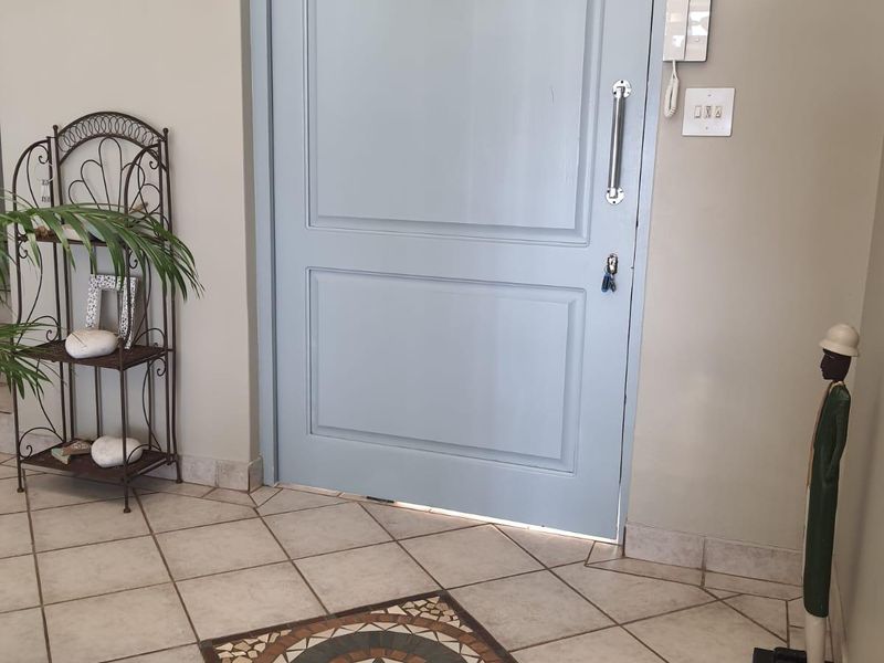A bright entrance foyer featuring light blue solid panel door, neutral tiled flooring with a decorative mosaic inlay, and a wall-mounted intercom system.