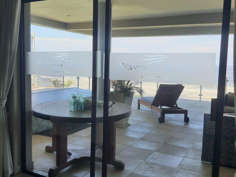A covered patio area featuring tiled flooring and a glass balustrade, offering direct access through large sliding doors with branded privacy film.
