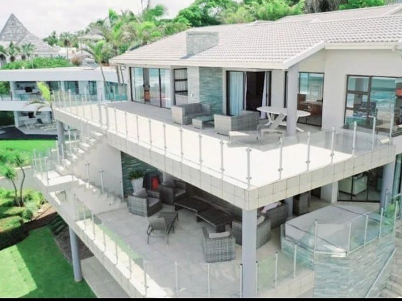 Elevated rear view of a modern multi-level home featuring expansive tiled patios, glass balustrades, and stone-clad architectural details overlooking a landscaped garden.