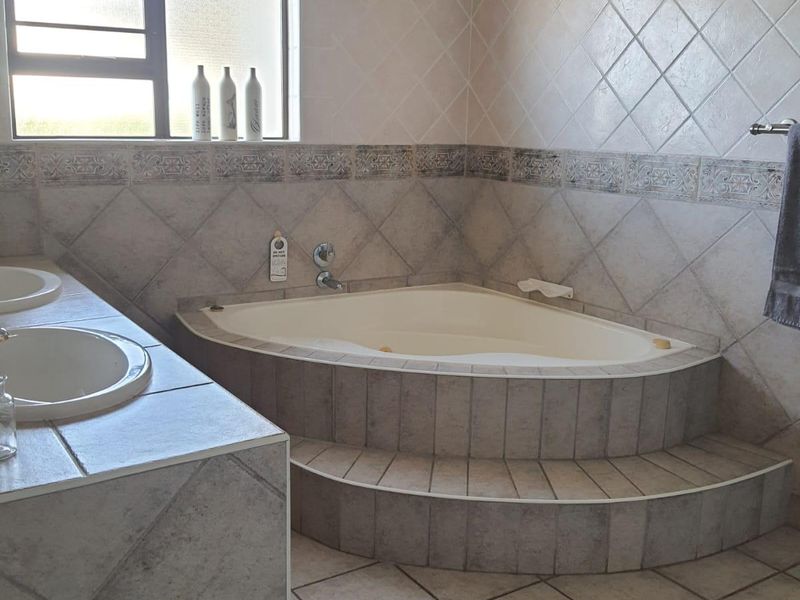 A functional bathroom featuring a corner bathtub, dual vanity sinks, and neutral tiled finishes throughout.