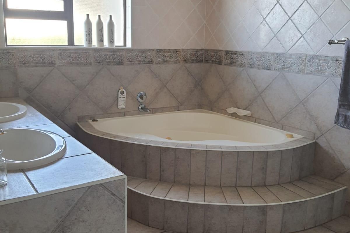 A functional bathroom featuring a corner bathtub, dual vanity sinks, and neutral tiled finishes throughout.