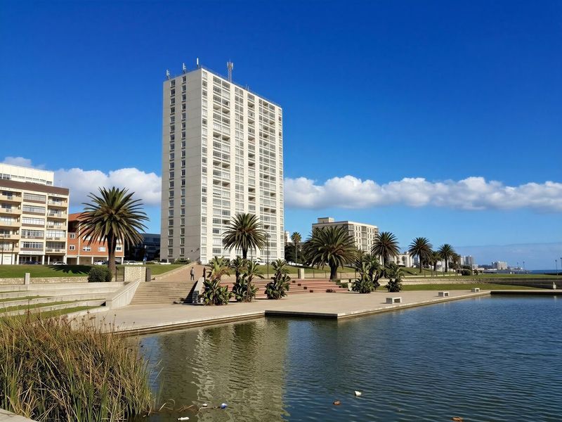 A view of a high-rise apartment building situated along a landscaped waterfront promenade with concrete walkways and stairs.
