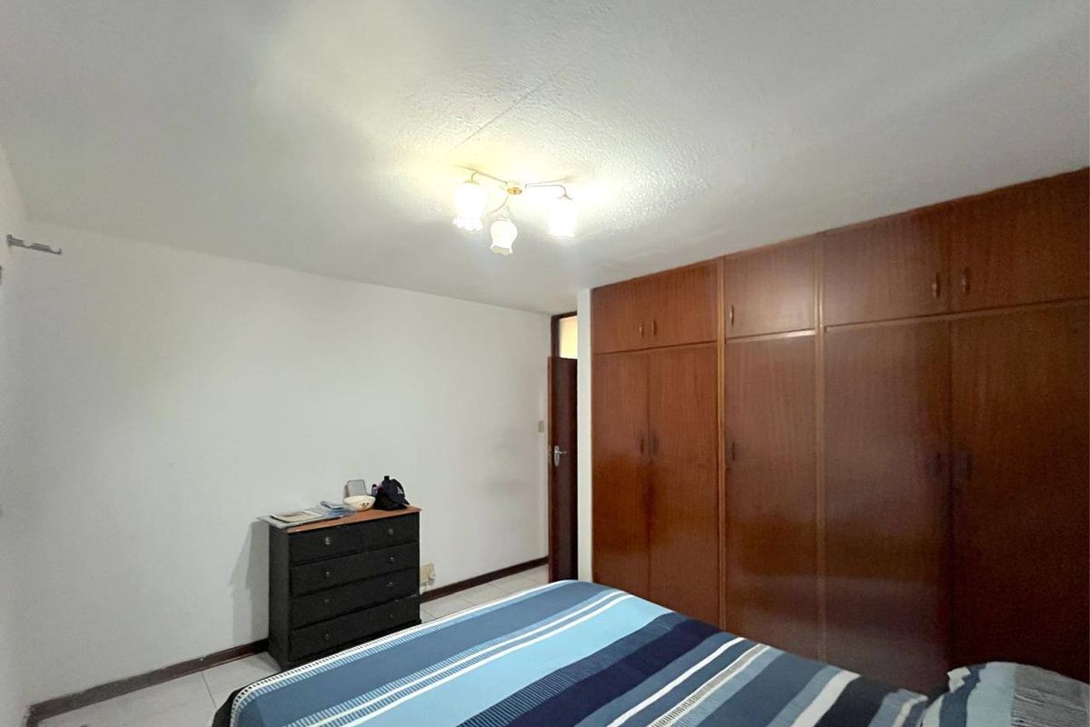 A bedroom featuring built-in wooden wardrobes, tiled flooring, and a central ceiling light fixture.
