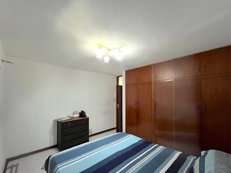A bedroom featuring built-in wooden wardrobes, tiled flooring, and a central ceiling light fixture.