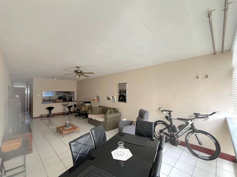 Spacious open-plan living and dining area featuring tiled flooring, a ceiling fan, and a convenient pass-through window connecting to the kitchen.