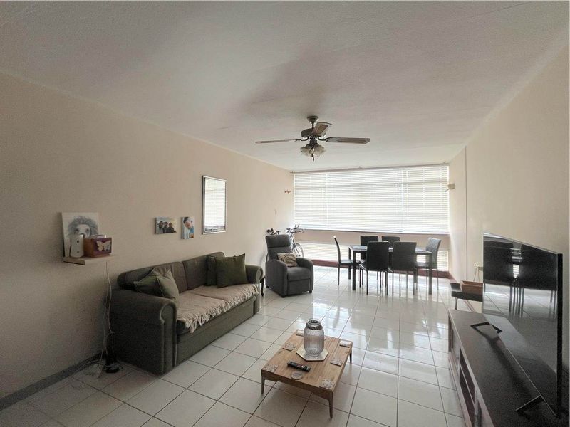 Spacious open-plan living and dining area featuring neutral tiled flooring, a ceiling fan, and large windows that provide ample natural light.