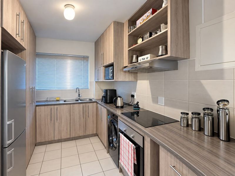 Modern galley-style kitchen featuring wood-look cabinetry, laminate countertops, integrated appliances, and neutral ceramic tile flooring with a functional layout.