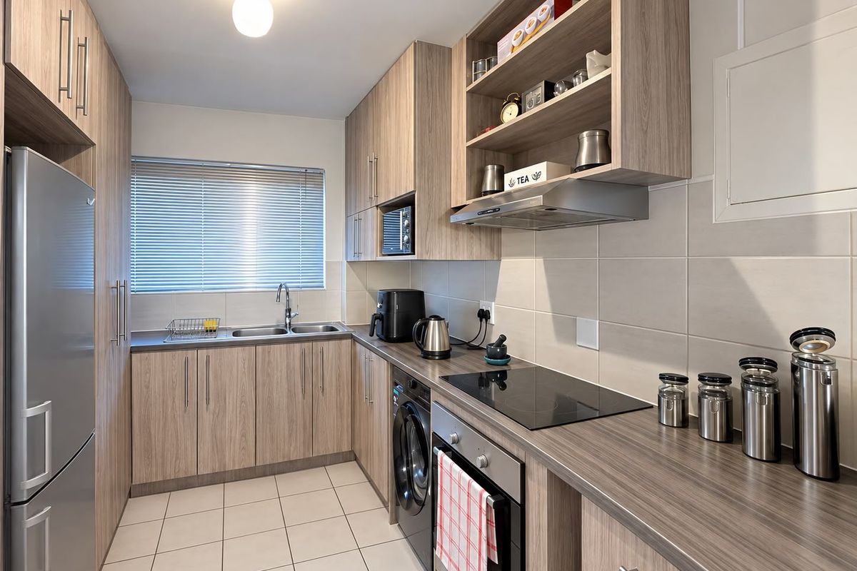 Modern galley-style kitchen featuring wood-look cabinetry, laminate countertops, integrated appliances, and neutral ceramic tile flooring with a functional layout.