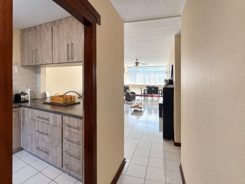 Open plan apartment layout featuring a functional kitchen with laminate cabinetry and tiled flooring, flowing into a bright living and dining area.