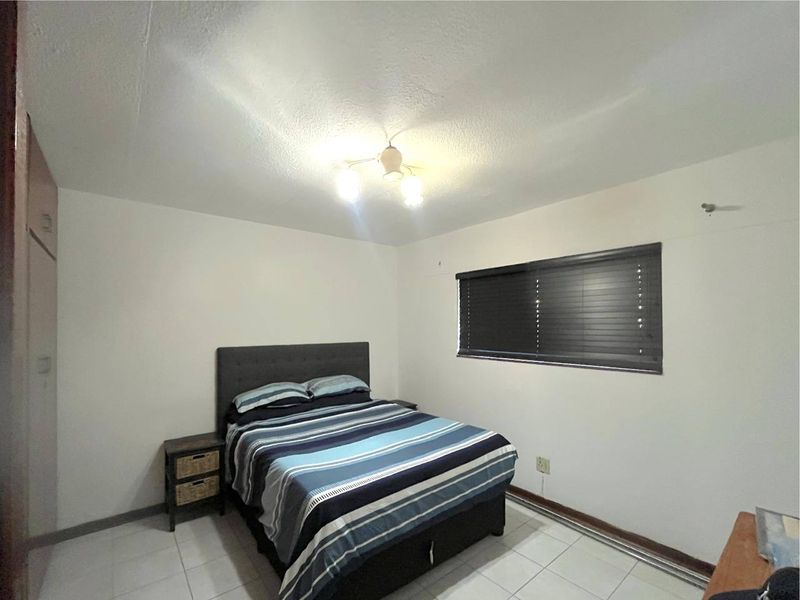 A functional bedroom featuring tiled flooring, a built-in wardrobe, and window blinds, offering a neutral space ready for personalization.