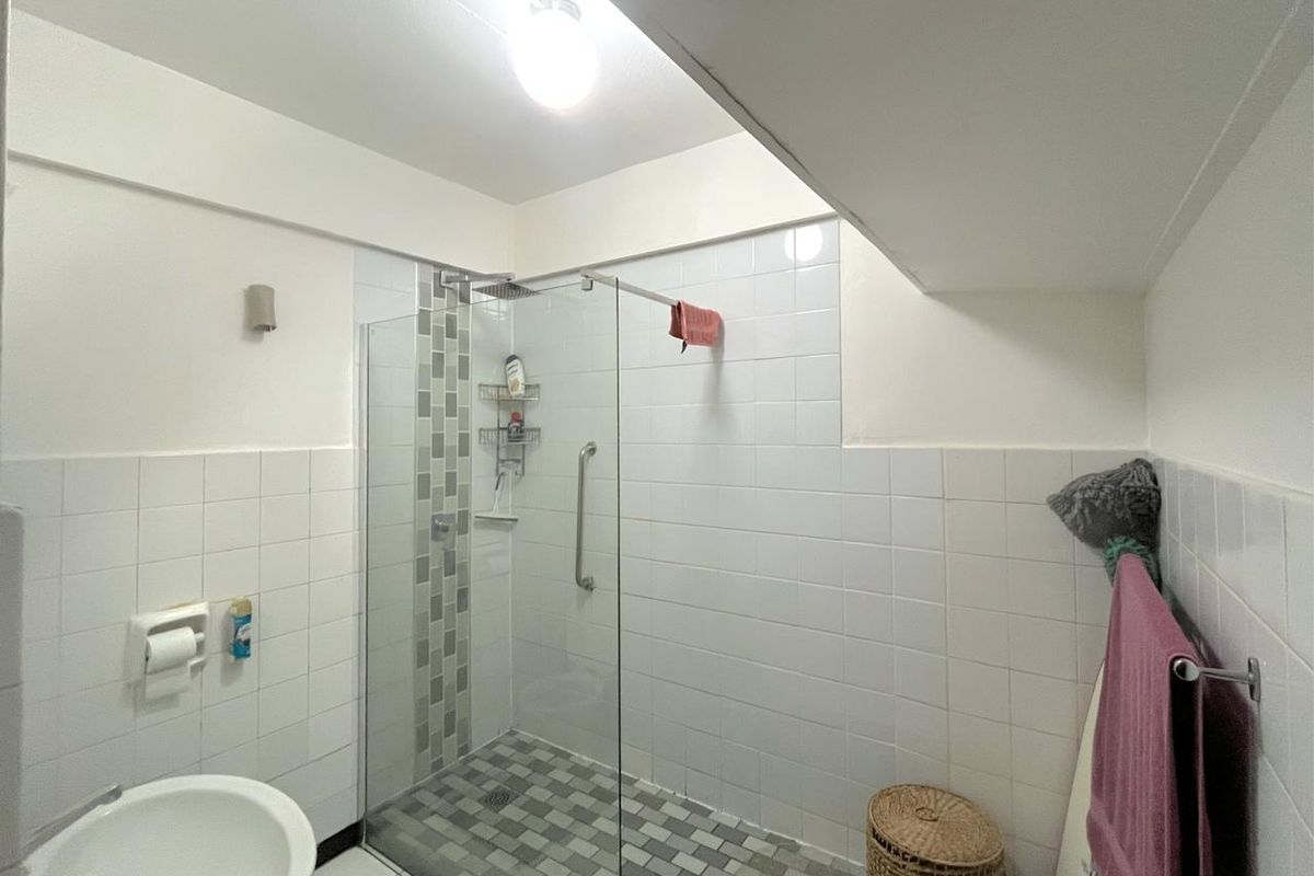 A functional bathroom featuring a walk-in shower with a glass screen, tiled flooring, and wall-mounted fixtures.