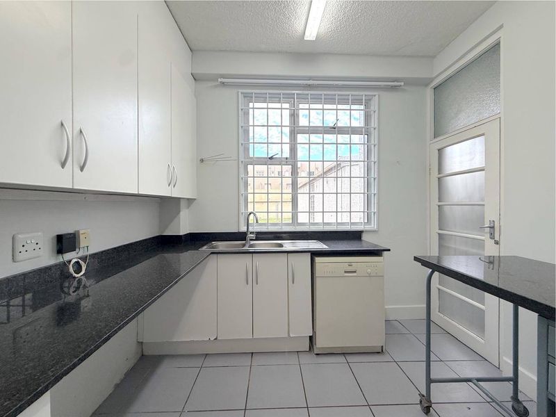 A functional scullery featuring white built-in cabinetry, dark granite countertops, a double sink, and tiled flooring with direct access to an exterior door.