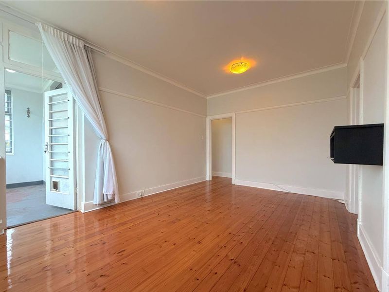 A bright and spacious living room featuring polished hardwood flooring, classic picture rails, and direct access to an adjoining balcony area.