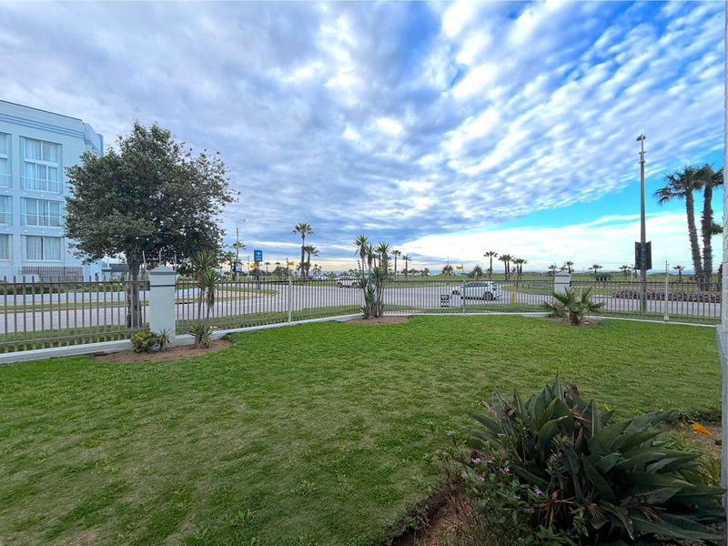 A well-maintained garden area featuring a manicured lawn and secure metal perimeter fencing, offering an open outlook towards the street and coastal surroundings.