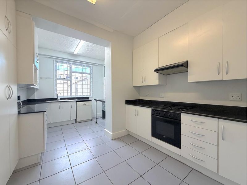 A clean, functional kitchen featuring white cabinetry, contrasting black granite countertops, built-in oven, gas hob, and tiled flooring.