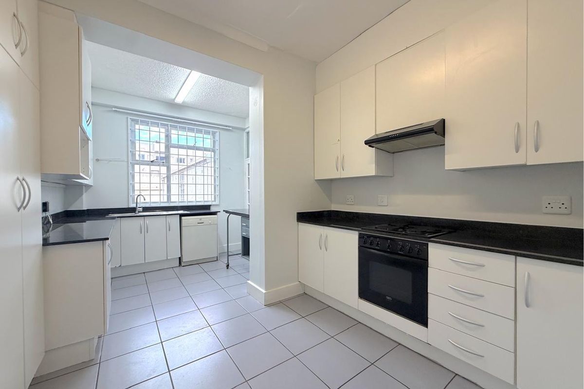 A clean, functional kitchen featuring white cabinetry, contrasting black granite countertops, built-in oven, gas hob, and tiled flooring.