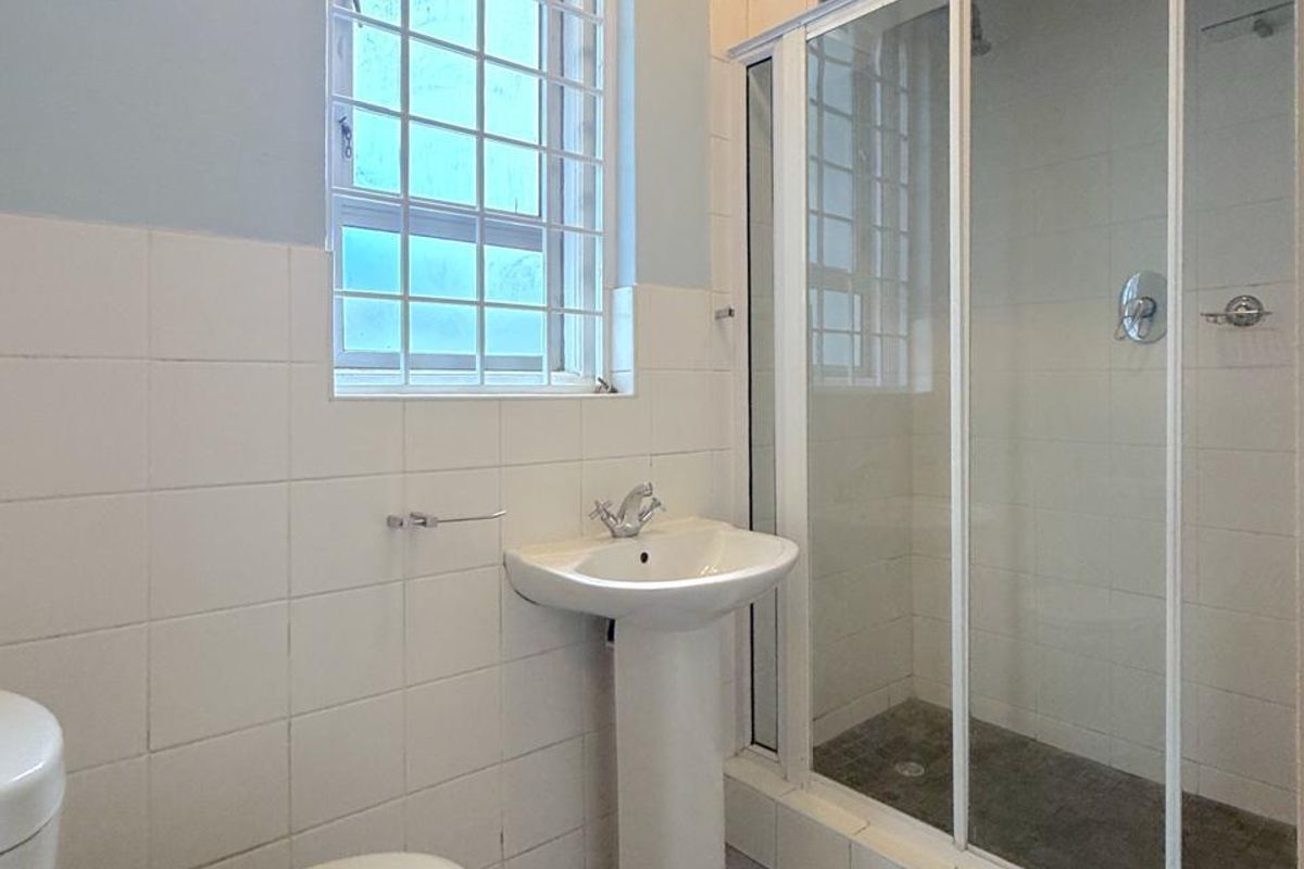 A functional bathroom featuring a pedestal basin, a glass-enclosed shower, and neutral wall and floor tiling.